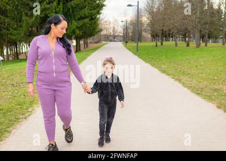 Jeune mère dans un parc de printemps avec la fille de 5s, s'amuser, la marche tenir la main dans la soirée.