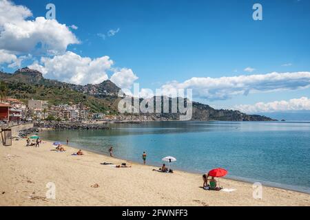 Des personnes non identifiées sur la plage de Giardini Naxos avec la ville de Taormina en arrière-plan, la Sicile Banque D'Images