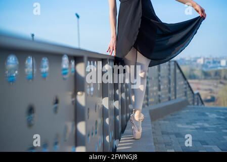 Ballerine dans les jambes de ballet en chaussures et tutu noir dansant près de la clôture. Belle jeune femme en robe noire et pointe danse à l'extérieur. Magnifique Banque D'Images