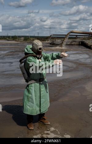 Un écologiste masculin dans un costume de protection vert et un masque à gaz prend un échantillon d'eau dans un lac pollué. Déchets de production. Un scientifique fait un Banque D'Images