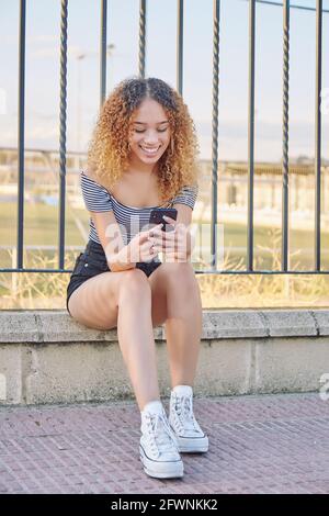 Jeune fille latina souriante tenant un smartphone à l'aide de la technologie d'application mobile à la maison. Bonne jeune fille hispanique textant, en vérifiant les applications de médias sociaux. Photo de haute qualité Banque D'Images