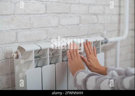 Une femme portant un pyjama chauffe les mains froides sur le radiateur de chauffage Banque D'Images