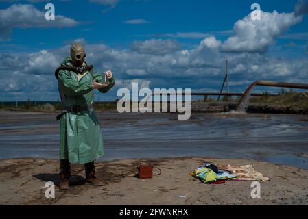 Un écologiste masculin dans un costume de protection vert et un masque à gaz prend un échantillon d'eau dans un lac pollué pour la recherche. Production de déchets. Scientifique Banque D'Images