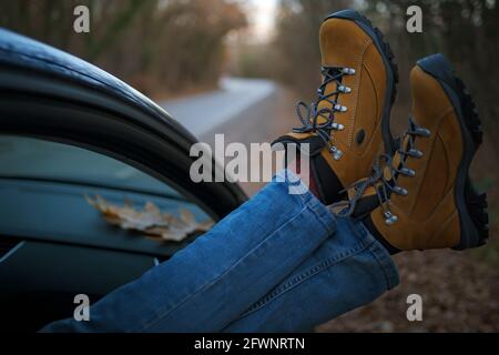 Femme pieds dans des bottes de randonnée jaune tendance sur la porte de voiture. Pieds à l'extérieur de la fenêtre au coucher du soleil forêt. Le concept de liberté de mouvement. Un week-end d'automne Banque D'Images