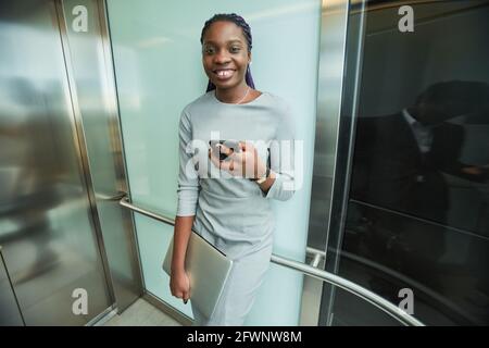 Portrait en œil de poisson d'une jeune femme d'affaires afro-américaine souriant à la caméra tout en se tenant dans un ascenseur, dans un espace de copie Banque D'Images