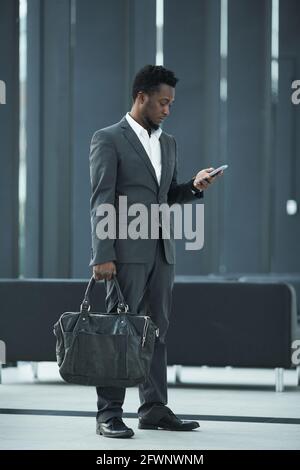 Portrait vertical complet d'un homme d'affaires afro-américain réussi à l'aide d'un smartphone dans un immeuble de bureaux Banque D'Images