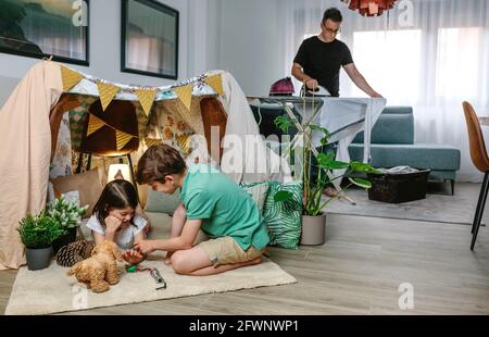 Père repassant pendant que ses enfants jouent au camping à la maison Banque D'Images