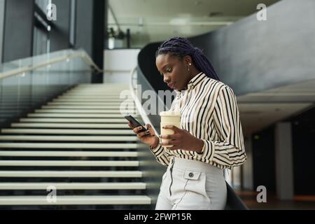 Portrait en vue latérale d'une jeune femme afro-américaine utilisant un smartphone dans une salle de bureau, un espace de copie Banque D'Images