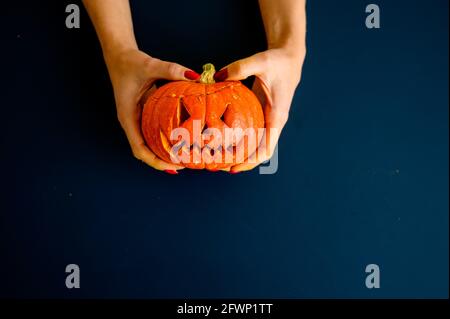 La femme tient une petite citrouille avec une grimace maléfique sur fond noir. Halloween concept, plat, vue de dessus. Le processus de fabrication de la citrouille-lanterne Banque D'Images