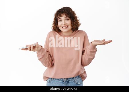 Désolé, mon erreur. Sourire coy fille haussant les épaules, tenant le téléphone mobile et semblent innocentes et sans indice, ne sais rien, n'ont rien à Banque D'Images