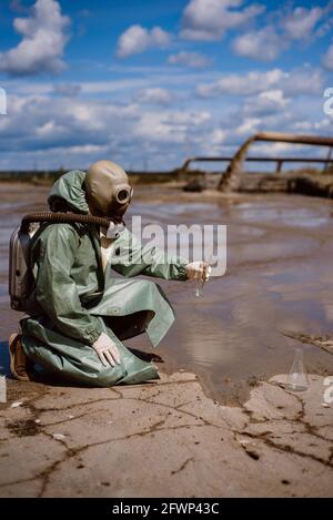 Un scientifique prélève un échantillon d'eau après le rejet de déchets chimiques. Un homme dans un respirateur et une combinaison de protection verte contre les radiations. Eau Banque D'Images