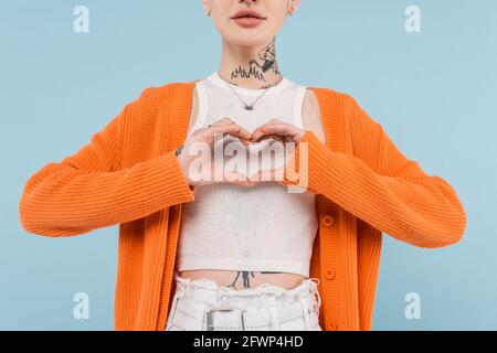 vue courte d'une jeune femme tatouée dans un gilet orange coeur avec mains isolées sur bleu Banque D'Images