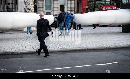 Les touristes se tenant entre deux sculptures géantes à deux doigts tandis que l'homme marche En observant à Trafalgar Square Banque D'Images