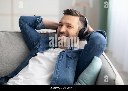Un homme à barbe heureux s'est couché sur un canapé avec un casque sans fil Banque D'Images