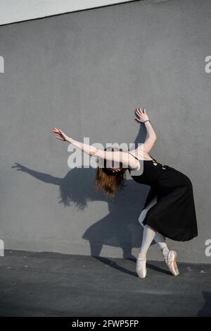 Ballerine en tutu debout près du mur. Belle jeune femme en robe noire et pointe danse à l'extérieur. Superbe ballerine exécutant un Banque D'Images