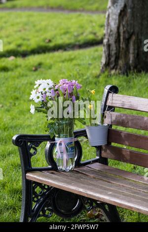 Fleurs laissées sur un banc en mémoire pour un être cher dans un parc. Banque D'Images