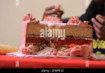 KAMPALA, OUGANDA - 20 avril 2021 : gâteau d'anniversaire et de fête en tranches avec les mains des Noirs dans le fond flou Banque D'Images