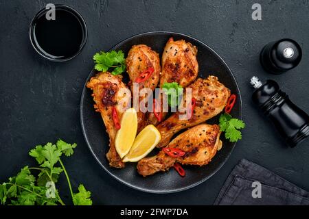 Bâtonnets de poulet grillé ou jambes ou barbecue grillé avec épices et sauce tomate salsa sur une assiette noire. Vue de dessus avec espace de copie. Banque D'Images