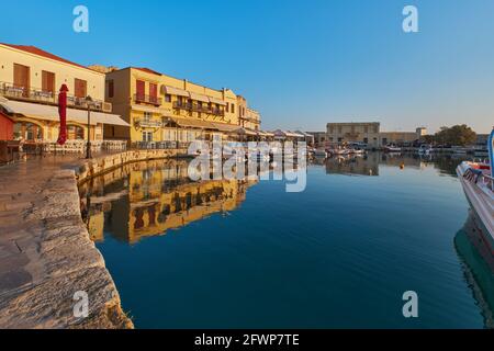 Le quai du port historique de Rethimno au soleil du matin, les bateaux dans le port et les restaurants vides Banque D'Images