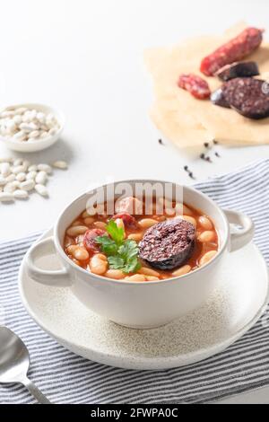 Asturiana fabada traditionnelle avec haricot, saucisse de sang sur une table blanche. Orientation verticale. Cuisine espagnole. Gros plan. Banque D'Images