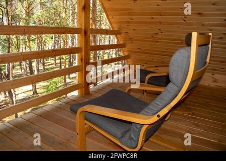 Vue sur une forêt depuis le balcon d'un chalet moderne en bois avec deux fauteuils. Tourisme et vacances d'été concept. Maison en bois d'été dans une forêt de pins Banque D'Images