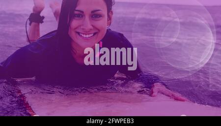 Composition de la surfeuse souriante couchée à la planche de surf dans l'eau avec lumière violette Banque D'Images