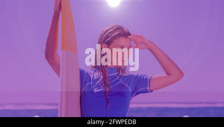 Composition de la femme souriante surfeuse tenant planche de surf sur la plage avec lumière violette Banque D'Images
