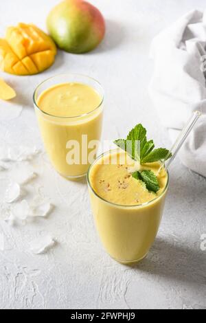 Deux lassi de mangue ou smoothies sur fond gris avec ombre ensoleillée. Boisson fraîche ayurvédique saine indienne à la mangue, au yaourt, à l'eau, aux épices, aux fruits et Banque D'Images