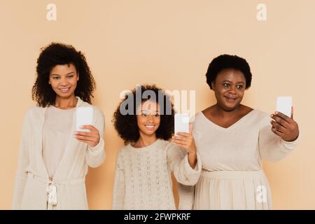 fille, petite-fille et grand-mère afro-américaine prenant des selfies sur un téléphone portable sur fond beige Banque D'Images