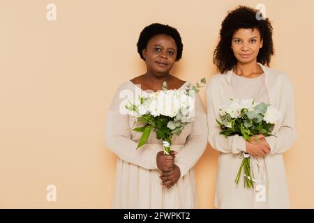 afro-américaines d'âge moyen et femmes adultes regardant la caméra avec bouquets de fleurs sur fond beige Banque D'Images