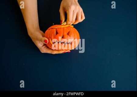 La femme tient une petite citrouille avec une grimace maléfique sur fond noir. Halloween concept, plat, vue de dessus. Le processus de fabrication de la citrouille-lanterne Banque D'Images