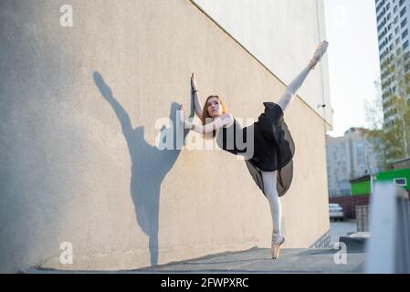 Ballerine en tutu debout près du mur. Belle jeune femme en robe noire et pointe danse à l'extérieur. Superbe ballerine exécutant un Banque D'Images