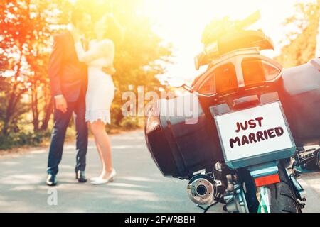 Mariage, jeunes mariés. L'arrière d'un vélo avec un panneau juste marié. Un homme et une femme dans des robes de mariage accosent et baiser debout sur la route, dans un flou dedans Banque D'Images