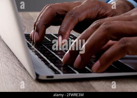 Gros plan d'un homme d'affaires utilisant un ordinateur portable sur une surface en bois contre arrière-plan gris Banque D'Images