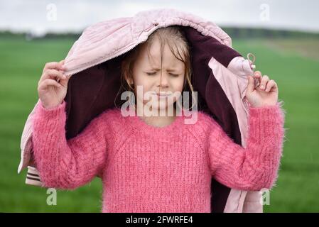 Fille cache sa tête sous une veste sous la pluie. Banque D'Images