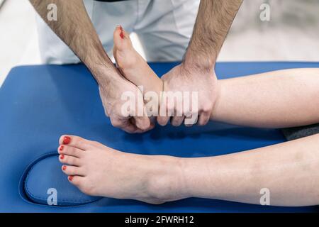 Un physiothérapeute masculin donne un massage des pieds à une femme non reconnue qui se trouve dans une civière. Banque D'Images