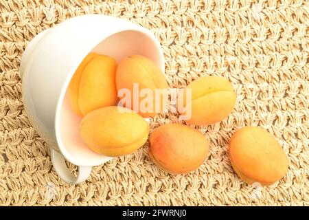 Plusieurs abricots jaunes d'ananas dans une tasse blanche, gros plan, sur un tapis de paille, vue de dessus. Banque D'Images