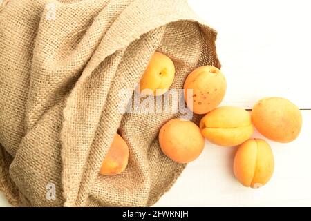 Plusieurs abricots jaunes d'ananas biologiques dans un sac de jute, gros plan, sur une table en bois blanc, vue de dessus. Banque D'Images