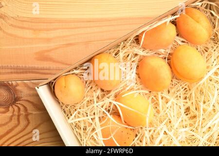 Plusieurs abricots mûrs d'ananas jaunes dans une boîte avec copeaux, gros plan, sur une table en bois, vue de dessus. Banque D'Images