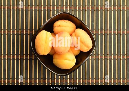 Plusieurs abricots jaunes d'ananas dans une assiette, gros plan, sur un tapis de bambou, vue de dessus. Banque D'Images