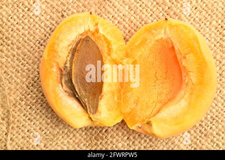 Un abricot jaune ananas coupé en deux, macro, sur le tissu jute, vue du dessus. Banque D'Images