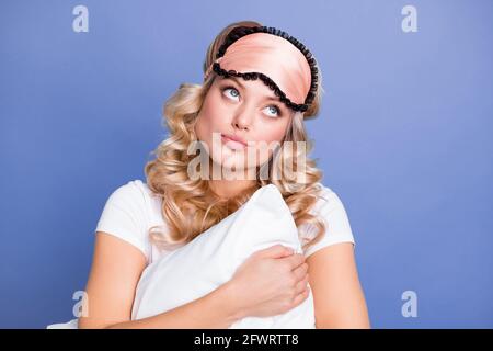 Portrait d'une femme aux cheveux ondulés rêveux et attirante qui s'embrasse en pensant à l'oreiller isolé sur fond bleu pastel Banque D'Images