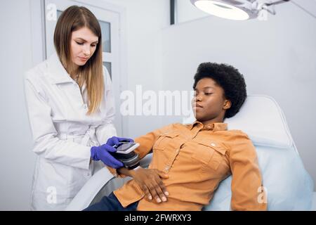 Prévention du cancer de la peau et du mélanome. Un médecin dermatologue professionnel examine les grains de beauté du patient sur le bras de la femme africaine à l'aide d'un dispositif moderne pour la dématoscopie Banque D'Images