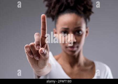 Stern a concentré sa jeune femme en tenant son index comme si elle mettait l'accent sur un point, en appelant à un arrêt ou en s'identifiant sur un backgroun gris studio Banque D'Images