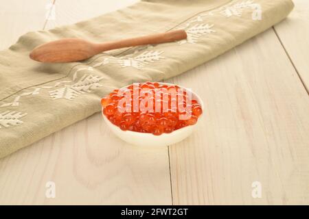 Caviar rouge biologique naturel dans un plat en céramique avec une serviette en lin et une cuillère en bois, gros plan, sur une table en bois blanc. Banque D'Images