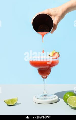 Verser le cocktail Strawberry Margarita dans un verre sur fond bleu moderne avec podium. Orientation verticale. Fraîcheur boisson alcoolisée d'été. Banque D'Images