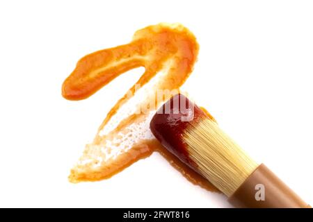 Brosse culinaire en bois trempée dans une sauce barbecue isolée sur un Arrière-plan blanc Banque D'Images