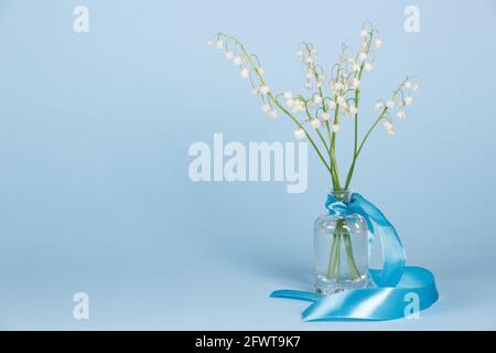 Bouquet de beaux lys frais de la vallée dans un vase en verre sur fond bleu Banque D'Images