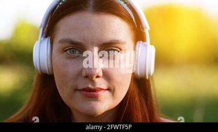 Belle femme qui écoute de la musique à l'aide d'un casque sans fil et d'un smartphone dans le parc de la ville Banque D'Images