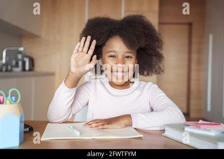 Bonne mixte-race préteen fille élève d'école levant la main sur en ligne leçon Banque D'Images